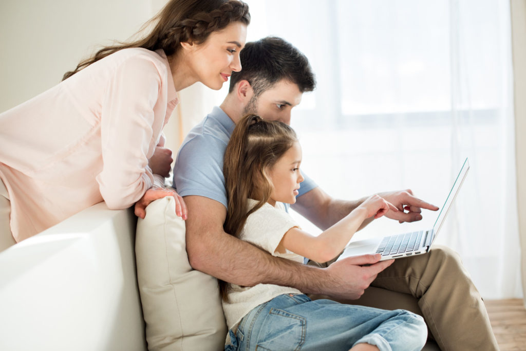 side view of parents and daughter using laptop at home
