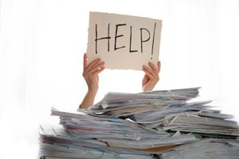 Person under a pile of papers with a hand holding a sign of help.